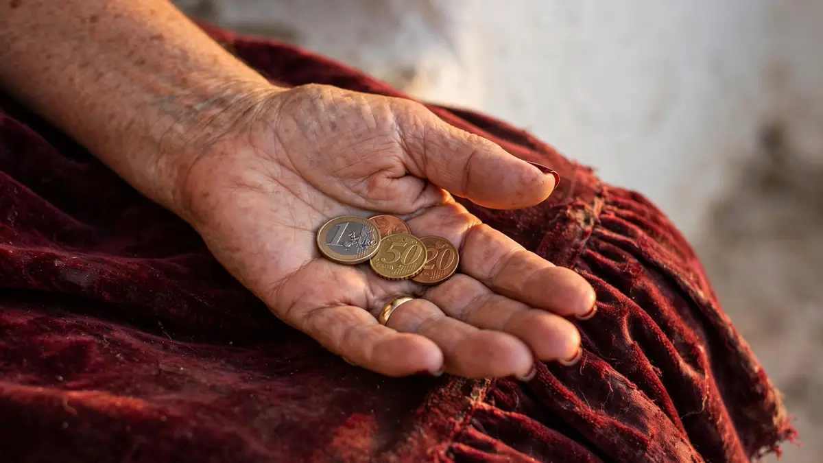 La mano abierta de Nerea, con las uñas rojo oscuro y la alianza, con unas monedas en la palma sobre la mesa camilla
